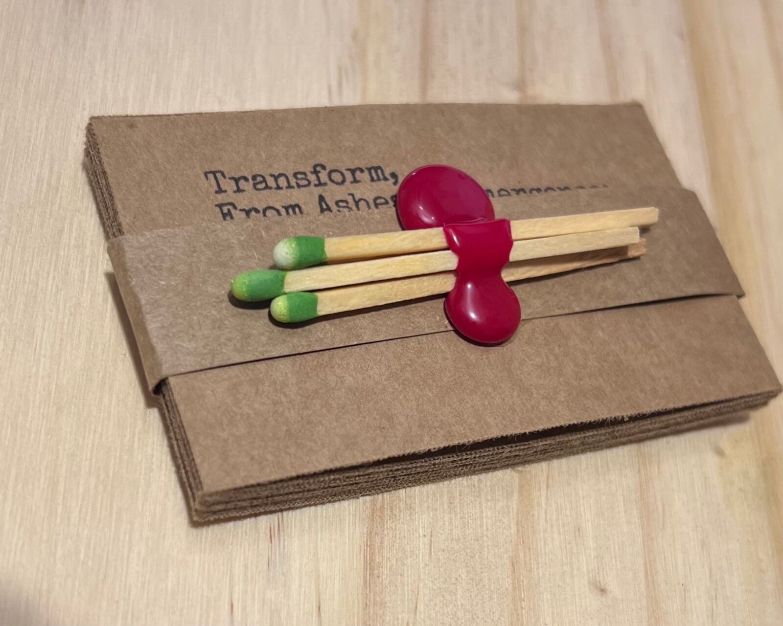 A banded stack of burn cards, the top one reading Transform, From Ashes to Emergence, with three green-tipped matches held on by a drip of red wax