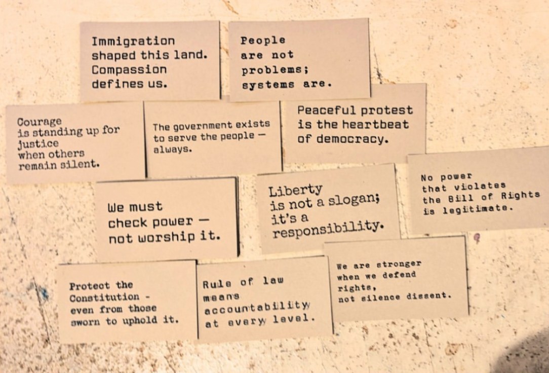 Thirteen democracy cards laid out on a plaster wall, including Peaceful protest is the heartbeat of democracy, and We must check power, not worship it