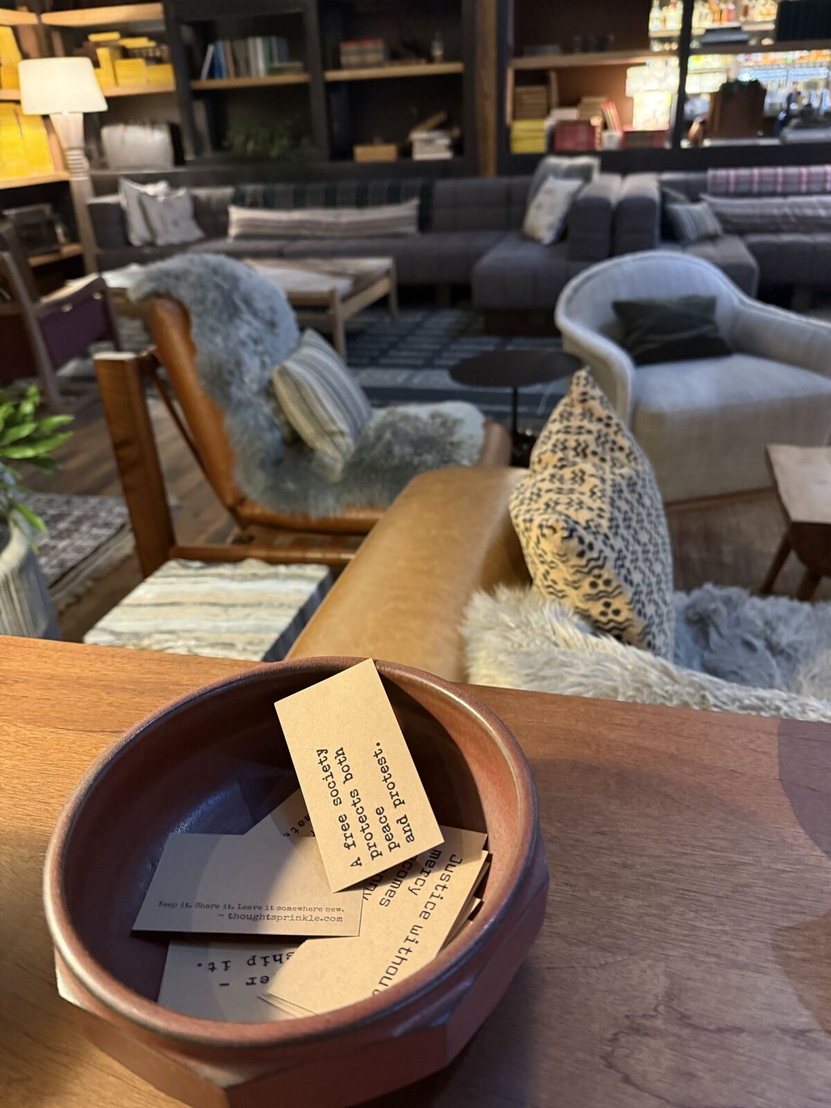 A clay bowl of kraft cards on a table in a hotel lobby. The top card reads: A free society protects both peace and protest.