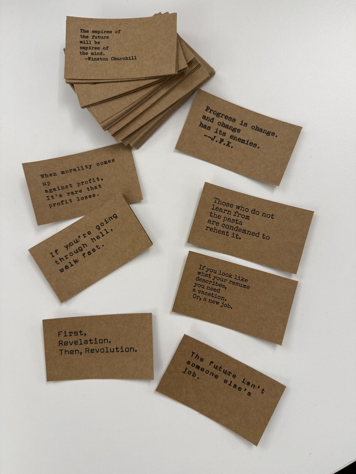 A fanned stack and eight loose kraft cards on a white table, including Churchill and JFK quotes